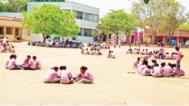 Students eating while sitting on the dirt floor in the sun